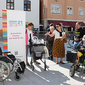 Eine Gruppe Menschen mit Rollstühlen, Rollator und Langstöcken, sowie ein Rollup der Agenda-Gruppe Menschen mit Behinderung.