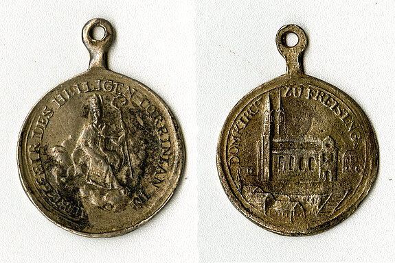 Erinnerung an 1824: eine kleine Medaille, die auf der Vorderseite den heiligen Korbinian und auf der Rückseite eine sehr schematische Darstellung des Freisinger Doms zeigt.