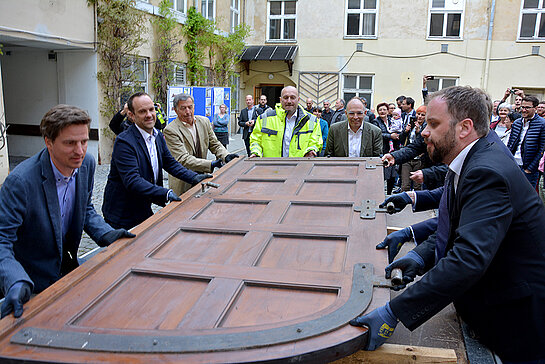 Der schwere Torflügel des Asamgebäudes wird mit vereinten Kräften auf ein Bauhof-Fahrzeug gehievt. 