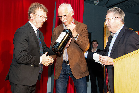 Kulturreferent Hubert Hierl und Musikschulbeirat Jürgen Maguhn (v.r.) überreichen Martin Keeser eine extra große Flasche Rotwein für weitere Inspirationen. (Foto: Stadt Freising)