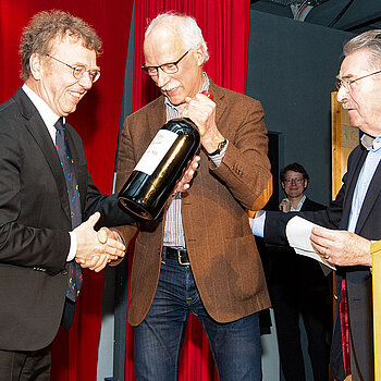 Kulturreferent Hubert Hierl und Musikschulbeirat Jürgen Maguhn (v.r.) überreichen Martin Keeser eine extra große Flasche Rotwein für weitere Inspirationen. (Foto: Stadt Freising)