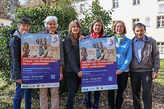 vier Frauen und ein Mann halten 2 Ausstellungsplakate hoch und stehen im Grünen
