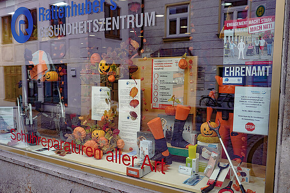 Herbstdeko mit Blättern, Kürbis und Lampionblumen, dazu Plakate mit Infos im Schaufenster