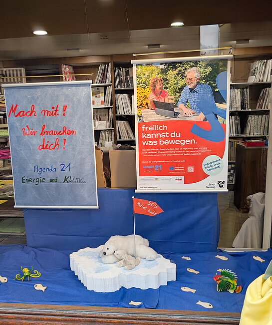 Engagement fürs Klima - die Agenda21 Energie und Klima bei Thalhuber. Foto: Stadt Freising in einem Fenster liegt blauer Stoff aus, darauf Meerestiere und eine Eisscholle mit Eisbären. Dazu das Plakat: Mach mit! Wir brauchen Dich!