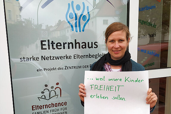 Veronika Unterreithmeier steht vor dem Elternhaus und hält ein Schild mit dem Text: "...weil unsere Kinder FREITHEIT erleben sollen." 