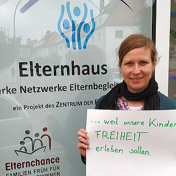 Veronika Unterreithmeier steht vor dem Elternhaus und hält ein Schild mit dem Text: "...weil unsere Kinder FREITHEIT erleben sollen." 