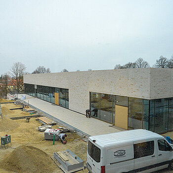 Blick durch ein Fenster auf die Turnhalle und die laufenden Arbeiten für die Freiflächen. (Foto: Stadt Freising)