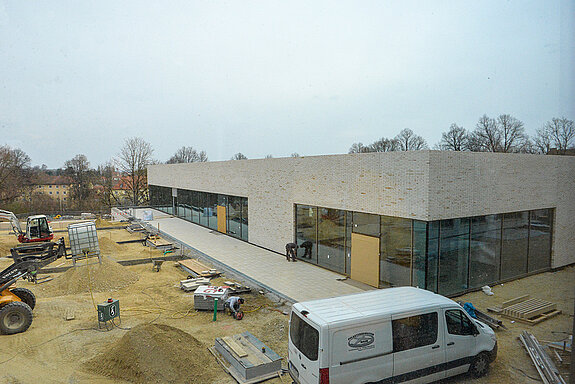 Blick durch ein Fenster auf die Turnhalle und die laufenden Arbeiten für die Freiflächen. (Foto: Stadt Freising)