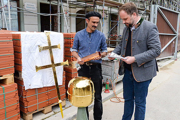 OB Tobias Eschenbacher befüllt den Kupferbehälter mit einer Baubescheibung der laufenden Generalsanierung, einem Zeitungsausschnitt des Richtfestes, aktuellen Münzen sowie einer Broschüre der ehemaligen Nutzer*innen. (Foto: Stadt Freising)