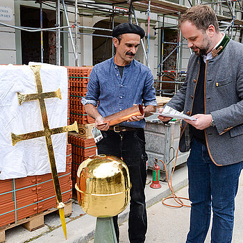 OB Tobias Eschenbacher befüllt den Kupferbehälter mit einer Baubescheibung der laufenden Generalsanierung, einem Zeitungsausschnitt des Richtfestes, aktuellen Münzen sowie einer Broschüre der ehemaligen Nutzer*innen. (Foto: Stadt Freising)