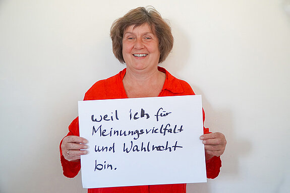 Stadtratsmitglied Charlotte Reitsam. Foto: Stadt Freising Eine Frau in einem orangenen Hemd zeigt ein Schild mit der Aufschrift "weil ich für Meinungsvielfalt und Wahlrecht bin."