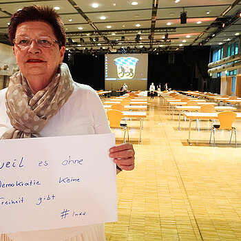 Bürgermeisterin Eva Bönig hält ein Schild mit der Aufschrift: "weil es ohne Demokratie keine Freiheit gibt"