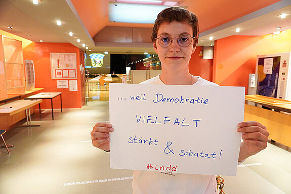 Stadträtin Joana Bayraktar hält ein Schild mit der Aufschrift: "Demokratie Vielfalt stärkt & schützt!"