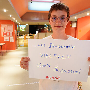 Stadträtin Joana Bayraktar hält ein Schild mit der Aufschrift: "Demokratie Vielfalt stärkt & schützt!"