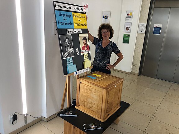 Wahlurne mit Plakat und einer Frau, die das präsentiert.