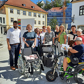 Eine Gruppe Menschen mit Rollstuhl, Rollator im Sonnenschein am Kriegerdenkmal Freising