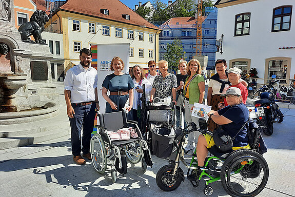 Eine Gruppe Menschen mit Rollstuhl, Rollator im Sonnenschein am Kriegerdenkmal Freising