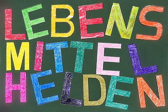 Bunte Gro&szlig;buchstaben in verschiedenen Farben, teilweise leicht schief auf einer Tafel