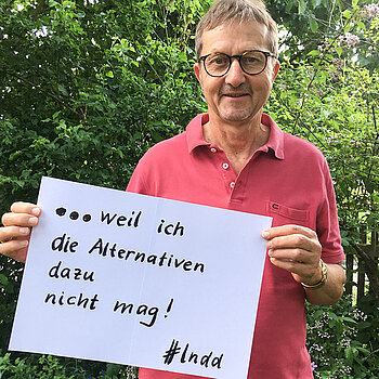 Johannes Schmuker steht vor einer Hecke und hält ein Schild mit der Aufschrift: " weil ich die Alternativen dazu nicht mag!" 