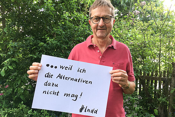 Johannes Schmuker steht vor einer Hecke und hält ein Schild mit der Aufschrift: " weil ich die Alternativen dazu nicht mag!" 