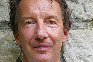 Professor Dr. Olaf Müller, Foto: Kalina Trzaska Portrait eines Mannes vor eine groben Steinmauer