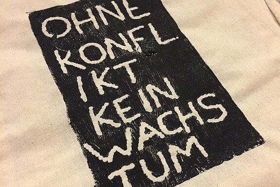 Auf eine Tasche gedruckt: "Ohne Konflikt kein Wachstum" Weiß auf schwarzem Grund