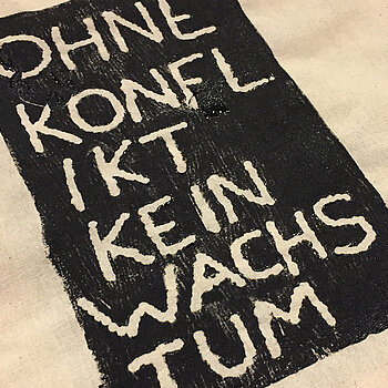 Auf eine Tasche gedruckt: "Ohne Konflikt kein Wachstum" Weiß auf schwarzem Grund