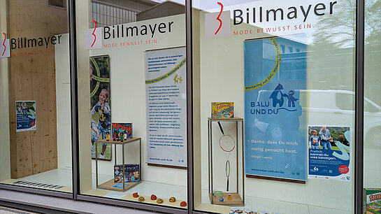 Mentoren gesucht (bei Billmayer): Balu und Du sucht junge Erwachsene für Freizeitaktivitäten mit Kindern. Foto: Stadt Freising In mehreren großen Fenstern hängen Banner mit Fotos und Infos, dazu Spiel- und Bastelmaterial