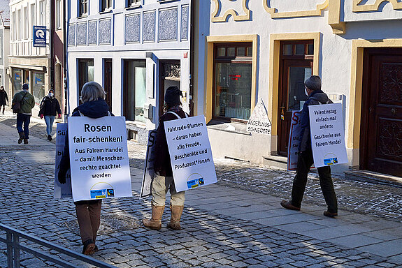 Drei Menschen mit Plakaten für Fairen Handel gehen durch die Straße.