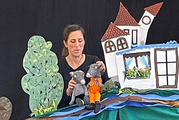 eine Frau mit Handpuppen in einer gemalten Kulisse