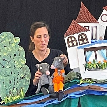 eine Frau mit Handpuppen in einer gemalten Kulisse