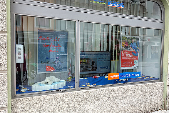 ein zweiteiliges Schaufenster mit Eisbär auf einer Scholle, Plakat und Bildschirm, der verschiedene Aktionen zeigt