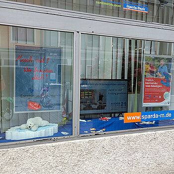 ein zweiteiliges Schaufenster mit Eisbär auf einer Scholle, Plakat und Bildschirm, der verschiedene Aktionen zeigt