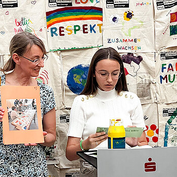 ein junges Mädchen und eine Frau vor einer Wand mit bedruckten Taschen 