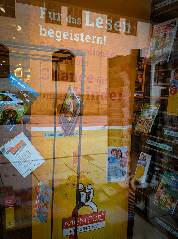 ein Orangefarbenes Rollup und davor Bücher hängend in einem Schaufenster.