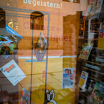 ein Orangefarbenes Rollup und davor Bücher hängend in einem Schaufenster.