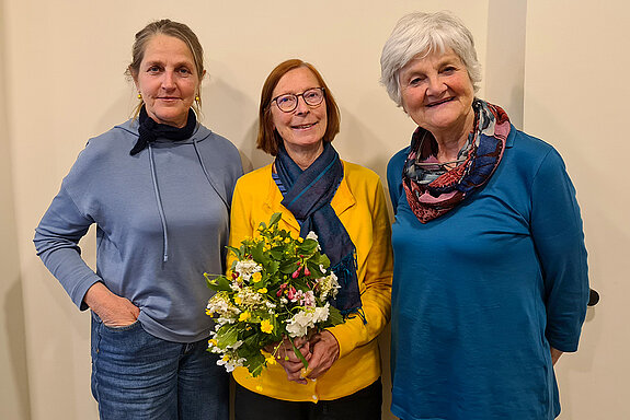 drei lächelnde Frauen, die mittlere mit einem Blumenstrauß in der Hand