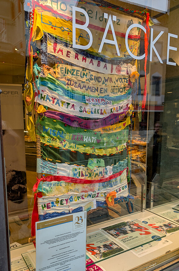 ein bunter Teppich aus Stoffstreifen in verschiedenen Sprachen. "Einzeln sind wir Worte, zusammen sind wir ein Gedicht."