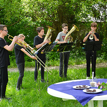 5 Schüler mit Blechblasinstrumenten vor Bäumen und Büschen