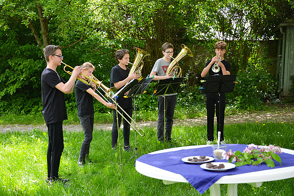 5 Schüler mit Blechblasinstrumenten vor Bäumen und Büschen