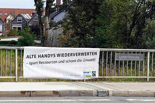 Ein Banner des Fairen Forums an der Luitpoldbrücke plädiert für ressourcenschonende Handynutzung.