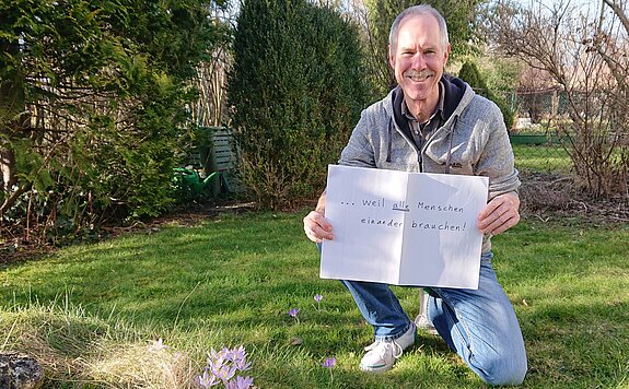 Niall Palfreyman hält ein Schild mit der Aufschrift: "... weil alle Menschen einander brauchen."