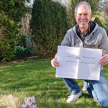 Niall Palfreyman hält ein Schild mit der Aufschrift: "... weil alle Menschen einander brauchen."