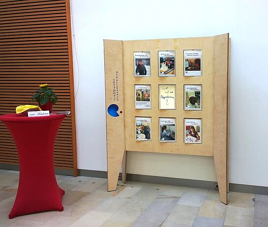 Ausstellungswand aus Holz mit beweglichen Elementen. Auf diesen sind Fotos und Texte zu Menschen, die sich engagieren. In der Mitte ein Spiegel mit der Aufschrift: "Lust auf ein Doppelleben?"