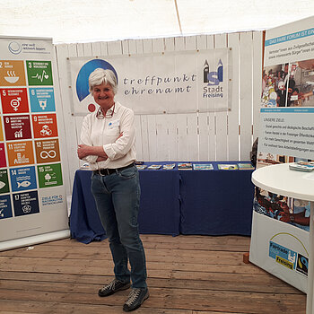 Eine Frau steht vor einem Rollup mit den bunten SDGs. Im Hintergrund ein Tisch mit Materialien