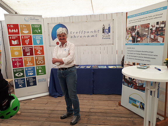Eine Frau steht vor einem Rollup mit den bunten SDGs. Im Hintergrund ein Tisch mit Materialien