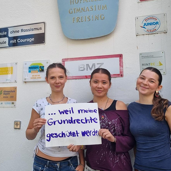 Amelia Herzer, Josefine Schimming und Mia Wengels feiern die Demokratie, weil die Grundrechte geschützt werden. Foto: Danzl Drei junge Frauen stehen vor dem Josef Hofmiller Gymnasium mit Schildern an der Wand. Unter anderem "Schule ohne Rassismus"