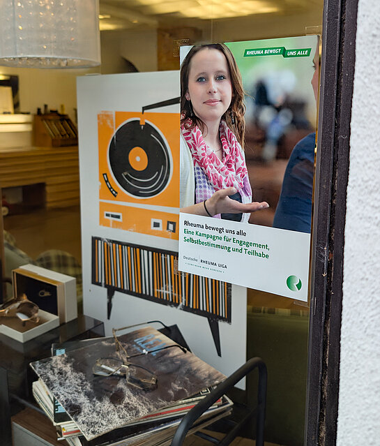 Rheuma bewegt uns alle. Rheumaliga bei Brillemacher. Foto: Stadt Freising Ein Plakat mit einer jungen Frau, im Hintergrund Schallplatten und eine Brille