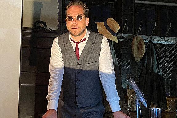 Ein Mann mit Sonnenbrille und rotem Schlips vor einer Garderobe.