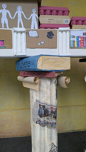Das geöffnete Tor. Detail der Installation des OMG Neufahrn. Foto: D. Lepkova Eine Säule aus Pappmaché, darauf ein Buch und weitere Elemente.